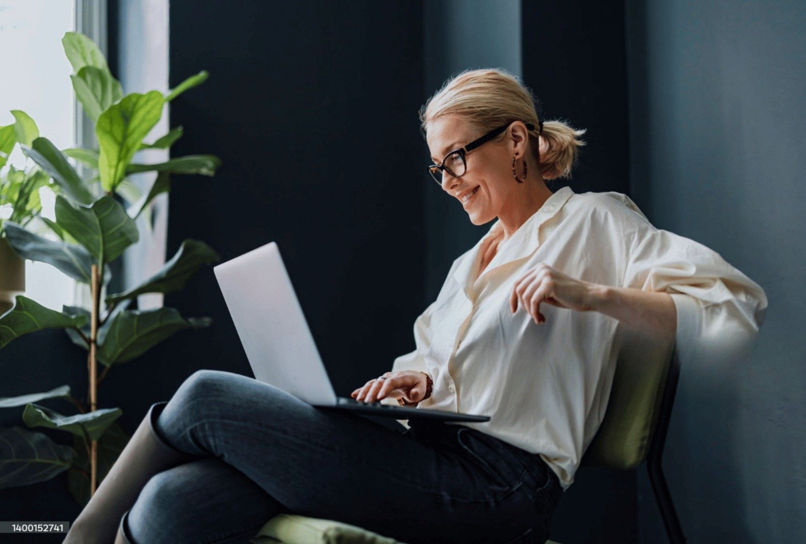 Mujer trabajando relajada en su laptop junto a una planta, transmitiendo claridad mental, equilibrio y bienestar